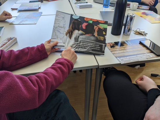 Jemand zeigt in einem Fortbildungs-Setting auf einen Folder